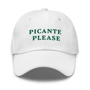 May include: A white baseball cap with the words "PICANTE PLEASE" embroidered in green. The cap has a curved brim and an adjustable strap at the back. This hat is a fun accessory.