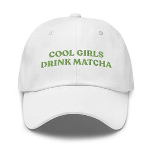 May include: White baseball cap featuring the green embroidered text "COOL GIRLS DRINK MATCHA". The cap has a curved peak and a classic six-panel design, ideal for everyday wear.