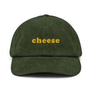 May include: A green corduroy baseball cap with the word "cheese" embroidered in yellow.