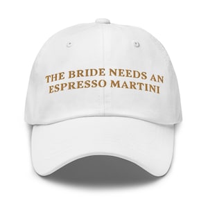 May include: White baseball cap with the text "THE BRIDE NEEDS AN ESPRESSO MARTINI" embroidered in brown.