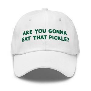 May include: White baseball cap with green embroidered text that reads "Are you gonna eat that pickle?"