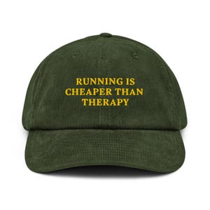 Op de afbeelding: Donkergroene corduroy baseballcap met de tekst "RUNNING IS CHEAPER THAN THERAPY" in het geel geborduurd. De cap heeft een gebogen klep en een gestructureerde kroon. Geschikt voor sport of vrije tijd.