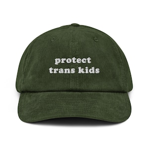 Könnte beinhalten: Eine dunkelgrüne Baseballkappe aus Cord mit weiß gesticktem Text, der "protect trans kids" lautet.