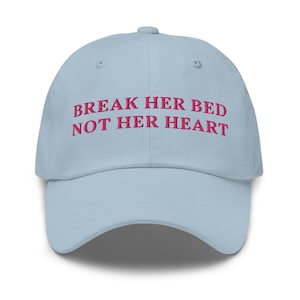 Puede incluir: Una gorra de béisbol azul claro con el texto "Break her bed not her heart" bordado en rosa.