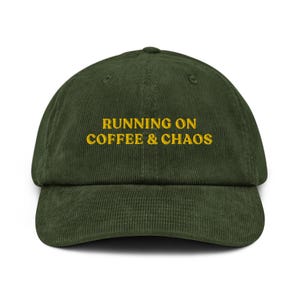 Puede incluir: Una gorra de béisbol de pana verde oscuro con el texto "RUNNING ON COFFEE & CHAOS" bordado en amarillo.