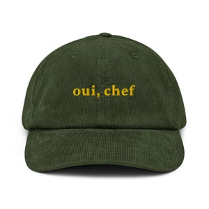 May include: A green corduroy baseball cap with the text "oui, chef" embroidered in yellow.