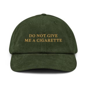 Op de afbeelding: Een groene corduroy baseballpet met de tekst "DO NOT GIVE ME A CIGARETTE" geborduurd in goud.