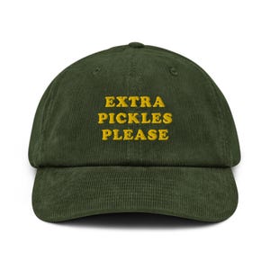 Op de afbeelding: Een donkergroene corduroy baseballpet met de tekst "EXTRA PICKLES PLEASE" geborduurd in geel.