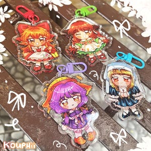 Puede incluir: Cuatro llaveros de personajes de estilo anime coloridos con detalles de purpurina. Cada llavero presenta un personaje diferente con un atuendo y un peinado únicos. Los llaveros están unidos a anillos de metal.
