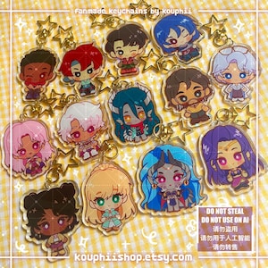 Puede incluir: Una colección de llaveros de acrílico con varios personajes de anime estilo chibi y cierres dorados en forma de estrella. El texto fanmade keychains by kouphii y kouphiishop.etsy.com es visible junto a un cuadro de advertencia.