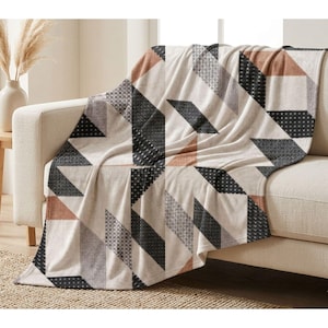 Può includere: Una coperta beige con un motivo geometrico di forme nere, grigie e color ruggine. La coperta è drappeggiata su un divano beige, creando un look accogliente ed elegante. La coperta è realizzata in un materiale morbido.