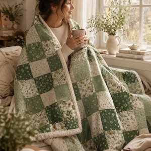 Könnte beinhalten: Eine Patchworkdecke mit einem grün-weißen Blumenmuster. Die Decke besteht aus Stoffquadraten in verschiedenen Grün- und Weißtönen mit einem weichen, flauschigen weißen Rand. Die Decke ist über eine Person drapiert.