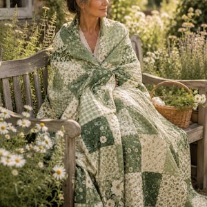 May include: A patchwork quilt with a floral and gingham pattern in shades of green and white. The quilt is draped over a wooden bench. A wicker basket with greenery sits nearby. The scene is set outdoors with flowers.