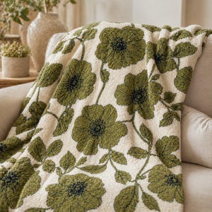 Könnte beinhalten: Eine cremefarbene Decke mit einem großen Blumenmuster in Grüntönen. Die Blumen haben dunkelmarineblaue Zentren und sind über die Decke verteilt. Die Decke ist über ein beiges Sofa drapiert.