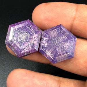 Peut inclure: Deux pierres précieuses violettes de taille hexagonale présentant un motif trapiche géométrique distinct avec des lignes rayonnantes et un cœur central. Les pierres ont une qualité translucide avec des inclusions internes visibles.