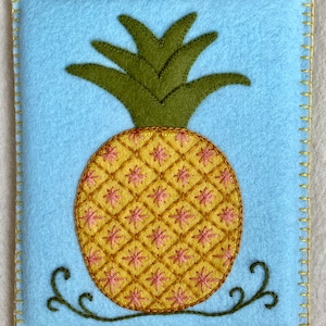 May include: A blue felt pouch with a yellow and pink embroidered pineapple design. The pineapple has green leaves and a brown stem.