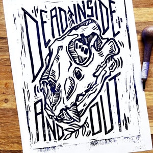 Könnte beinhalten: Ein Schwarz-Weiß-Linolschnitt eines Tierschädels mit dem Text "Dead Inside and Out" drumherum.