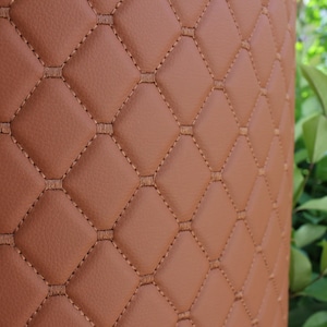 Könnte beinhalten: Nahaufnahme eines braunen Ledermaterials mit einem rautenförmigen Steppmuster.