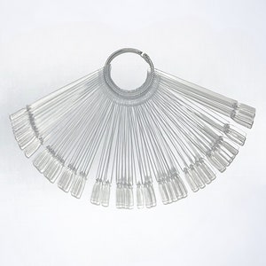May include: A clear plastic nail polish colour swatch fan with a silver metal ring. Each swatch is a rectangular shape with a rounded tip. The fan is spread out, displaying multiple colour options for nail polish.