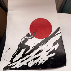 Peut inclure: Une impression linogravure en noir et blanc sur papier représentant la silhouette d'une figure poussant une grande forme circulaire rouge solide sur une pente raide et texturée. L'œuvre à fort contraste présente des lignes d'encre noire.