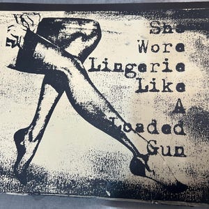 May include: Black and white illustration of a woman wearing lingerie. The text "She wore lingerie like a loaded gun" is printed on the image.