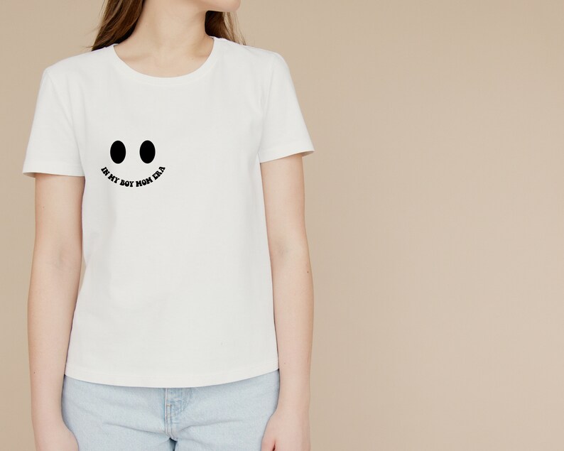 May include: White t-shirt with a black smiley face graphic and the text "In my boy mom era".