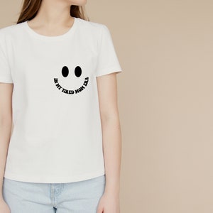 Pode incluir: Camiseta branca com um gr&aacute;fico de rosto sorridente preto e o texto "In my tired mom era".