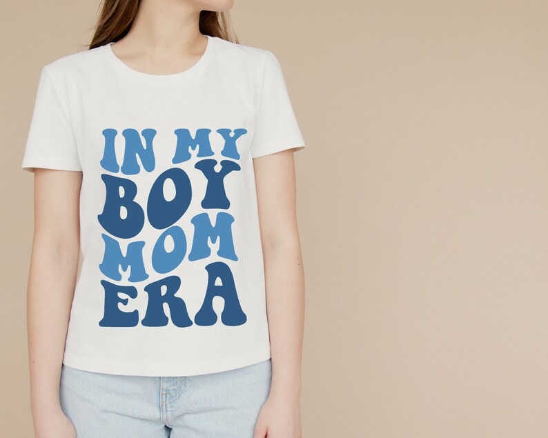 May include: White t-shirt with blue text that reads "In My Boy Mom Era" in a retro font.