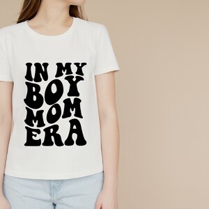 May include: White t-shirt with black text that reads "In My Boy Mom Era" in a retro font.