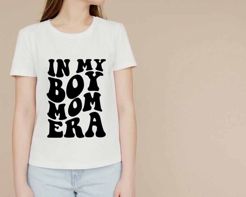 May include: White t-shirt with black text that reads "In My Boy Mom Era" in a retro font.