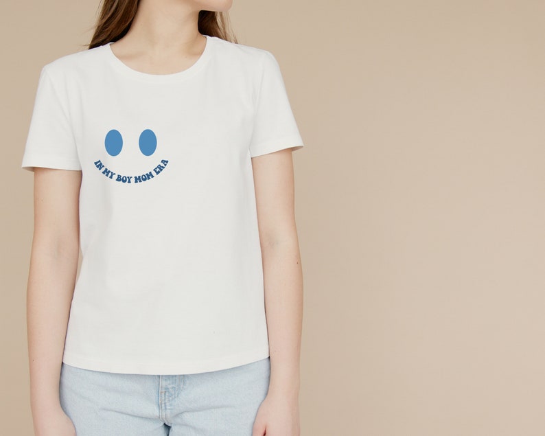 May include: White t-shirt with a blue smiley face graphic and the text "In My Boy Mom Era" printed on the front.