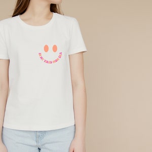 Pode incluir: Camiseta branca com um rosto sorridente rosa e laranja e o texto "In my tired, home era".