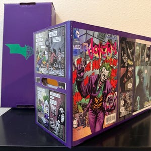 May include: A rectangular purple storage box decorated with comic book panels featuring the Joker. The front panel displays the Joker holding a gun with the text JOKER #1 and HA! HA! HA! repeated. A matching purple box lid stands vertically in the background.