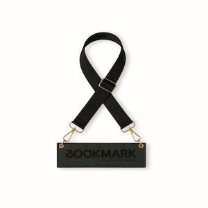 Könnte beinhalten: Schwarzer Lesezeichen mit dem Wort "BOOKMARK" auf einem dunkelgrünen rechteckigen Anhänger geprägt. Der Anhänger ist an einem schwarzen Riemen mit goldfarbener Metallhardware befestigt. Der Text "BY CORINE MARIE" steht darunter.