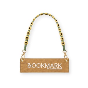Puede incluir: Un marcapáginas beige con la palabra "BOOKMARK" bordada en blanco, con "BY CORINE MARIE" debajo. El asa es verde con detalles de girasoles amarillos y marrones y cierres dorados.