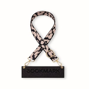 May include: A black and beige leopard print strap with gold-coloured metal fixings and a black rectangular tag that reads "BOOKMARK by CORINE MARIE". The strap is for a bag or purse.