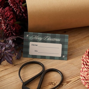 Könnte beinhalten: Ein rechteckiges Geschenkanhänger mit einem dunkelgrünen und schwarzen Karomuster und dem Text Merry Christmas in weißer Schreibschrift. Das Etikett enthält einen hellbraunen rechteckigen Bereich mit den Aufschriften FROM: und TO: sowie Linien.