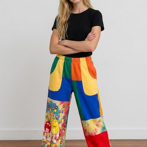 May include: A black short-sleeved t-shirt paired with loose-fitting patchwork sweatpants. The pants feature a vibrant color-blocked design in red, yellow, blue, and green, with a tie-dye section and a graphic print of red and yellow M&M characters.