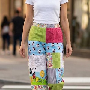 May include: A plain white short-sleeved t-shirt paired with patchwork trousers featuring a variety of colorful patterns, including polka dots, floral prints, stripes, and a graphic of Mickey Mouse, finished with simple white sneakers.