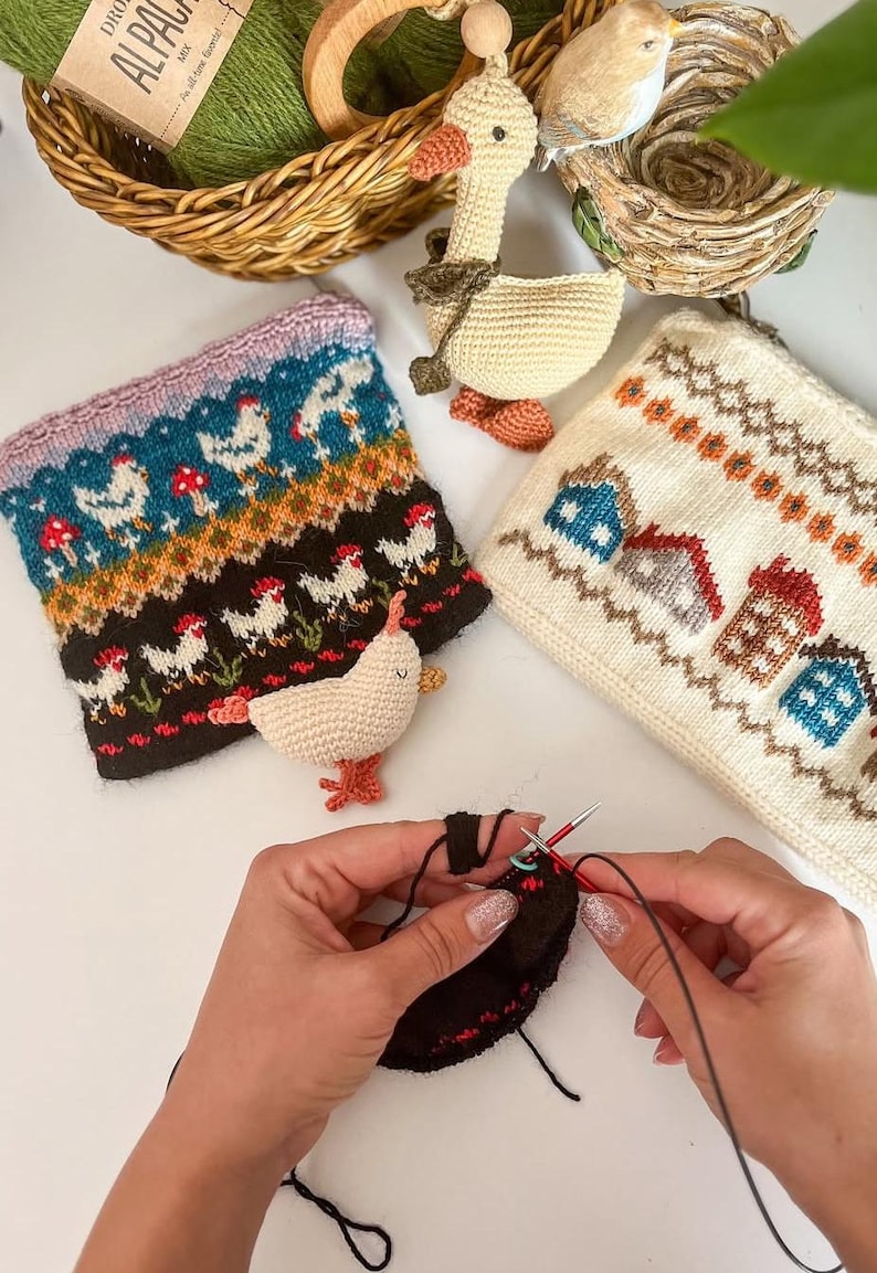 May include: A collection of handmade knitted items, including a chicken-themed cuff, a house-patterned pouch, and a crocheted duck. The image also shows a person knitting with black yarn and needles, showcasing the craft process.