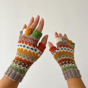 May include: A pair of fingerless gloves with a colorful geometric pattern in shades of brown, orange, yellow, green, blue, and white. The gloves are knitted and have a gray cuff.