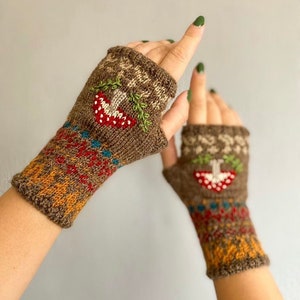 Puede incluir: Un par de guantes sin dedos marrones con un patrón de punto colorido y setas bordadas. Los guantes tienen un patrón marrón, naranja, rojo y azul.