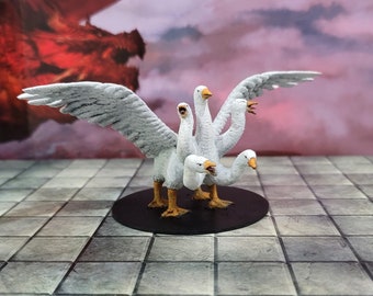May include: A white, multi-headed goose figurine with four heads and wings. The goose is standing on a black base.