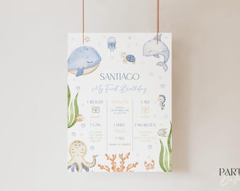 May include: A blue and white printable first birthday milestone sign with a watercolor ocean theme. The sign features a whale, octopus, seahorse, and other sea creatures. It includes spaces to fill in the child's name, weight, height, and other details.