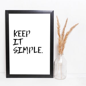Puede incluir: Impresión enmarcada en negro con el texto "KEEP IT SIMPLE." en blanco sobre fondo blanco. Un jarrón con hierba de la pampa seca está a la derecha de la impresión.