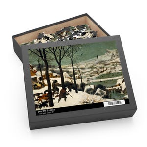 May include: A 16x20 inch puzzle box with a winter landscape scene. The box is open, revealing the puzzle pieces and the completed image. The image depicts figures in a snowy landscape with trees and buildings. The box also has text that reads "500 pcs Ages 9+".