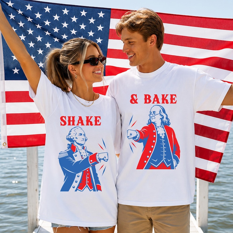 K&ouml;nnte beinhalten: Zwei wei&szlig;e T-Shirts mit rot-blauen Grafikdrucken historischer Pers&ouml;nlichkeiten. Ein Shirt zeigt George Washington mit dem Text SHAKE, das andere Benjamin Franklin mit dem Text & BAKE, beide in einer Faust-an-Faust-Pose.