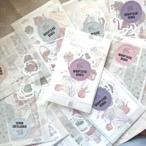 May include: Several clear cellophane bags filled with stickers, each sealed with a round sticker that reads "OOPSIE BAG". The stickers feature floral and botanical illustrations, including teacups, teapots, and flowers. The bags are arranged on a patterned surface.