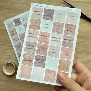 May include: Two sheets of planner tabs with watercolor-style backgrounds in shades of pink, brown, and beige. The tabs are labeled with months, days, and other planner categories. The text "Wildflower Soirée" is printed at the top of the sheets.