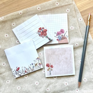 May include: Four different floral patterned sticky note pads. Each pad has a different design featuring a bouquet of flowers. The designs include a grid pattern, a lined pattern, a blank pattern with flowers along the bottom edge, and a blank pattern with flowers in the bottom right corner.
